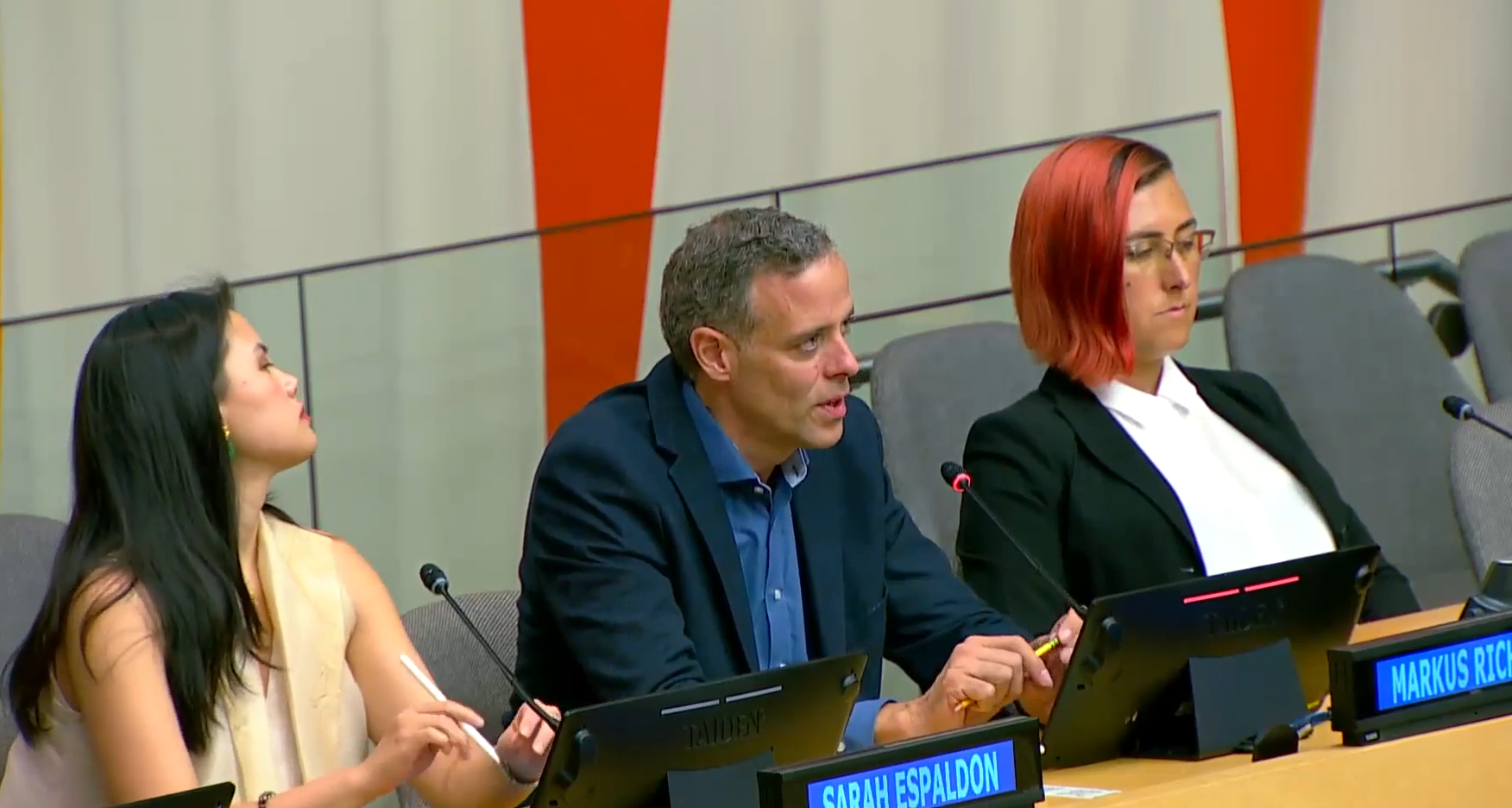 Three people in a panel, the middle person is speaking